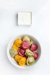 Multicolored dumplings in a bowl with sour cream.