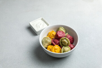 Multicolored dumplings in a bowl with sour cream.