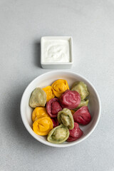 Multicolored dumplings in a bowl with sour cream.