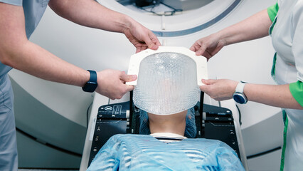 Specialists are preparing the young woman for radiation therapy by putting a special mask on him...