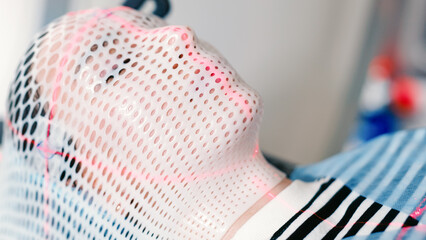 A young woman wearing an immobilization mask for radiotherapy lies in a CT capsule for precise diagnosis of the location of a tumor in the brain. Concepcion of modern medical technology.