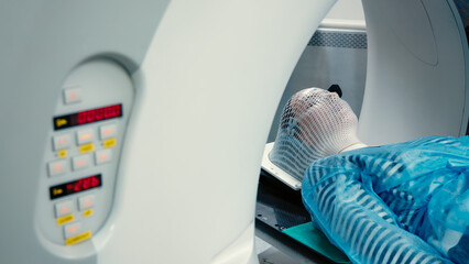 A young woman wearing an immobilization mask for radiotherapy lies in a CT capsule for precise diagnosis of the location of a tumor in the brain. Concepcion of modern medical technology.
