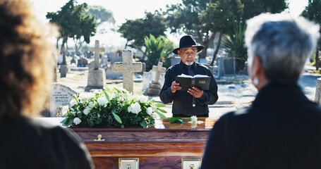 Bible, coffin and priest by graveyard with family for spiritual farewell, grief or loss. Religion,...