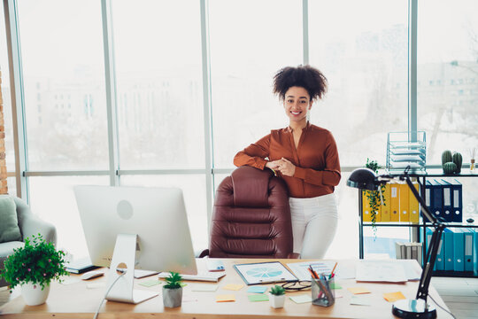 Confident businesswoman in modern office standing beside chair with creative workspace, emphasizing professional style and success