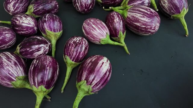 Fresh brinjals (eggplants) displayed at a vegetable chopping board, falling