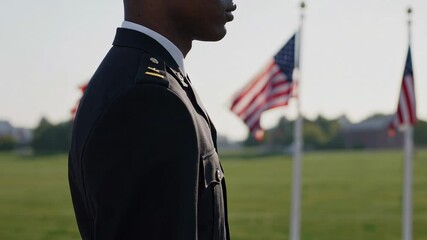 African american soldier stands respectfully at attention, his profile silhouetted against a backdrop of gently waving american flags on a grassy field, possibly during a commemorative event