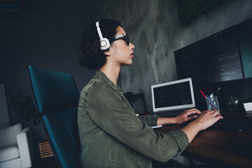 Young female coder working in a modern office environment with programming code on computers,...