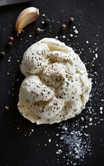 Delicious creamy burrata cheese garnished with black pepper and salt, served on a dark stone surface, perfect for culinary visuals.