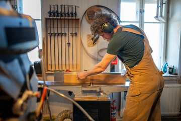 Focused attentive carpenter process wooden beam through jointer machine, preparing wood for final treatment. Surface smoothing and edge finishing, precise accuracy and readiness for woodworking