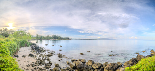 Tropical Rocky Coastline at Sunrise with Clear Waters and Lush Greenery. Panoramic View of a Serene Tropical Beach with Early Morning Sunlight