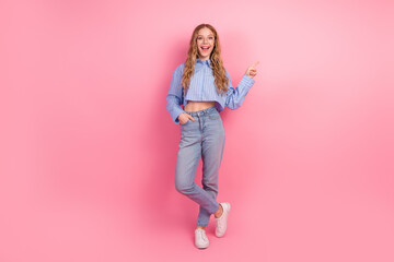 Young woman in casual outfit pointing to the side against pink background, cheerful and stylish...
