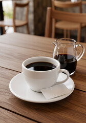 Fototapeta premium a simple white ceramic coffee cup and saucer on a wooden table, filled with black coffee. Next to the cup is a small clear glass carafe also containing black coffee