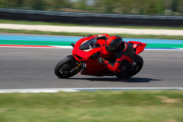 Rider in a red-black leather suit riding on a red sport motorcycle through a corner at a racing circuit at high speed and leaning from the bike.
