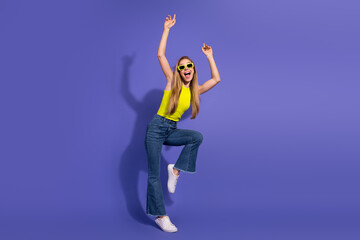 Young woman dancing happily while wearing trendy casual outfit on vibrant purple background