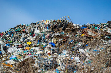 Mountains of waste clutter a landfill site, showcasing a variety of discarded materials against a clear blue sky