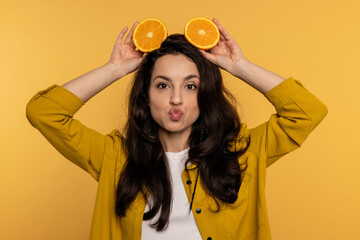 Mischievous woman posing for the camera on the yellow background with citrus fruit halves on her...