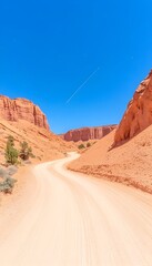 A winding dirt road cuts through a vibrant red rock desert canyon under a clear blue sky