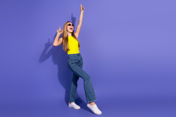 Fashionable young woman in a yellow top posing stylishly in front of a vibrant purple background,...
