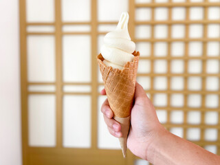 Hand holding Japanese milk flavored ice cream cone, soft white texture, sweet and refreshing taste.