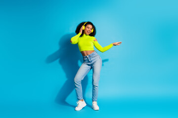 Young woman dancing joyfully wearing neon green top and jeans against vibrant blue background