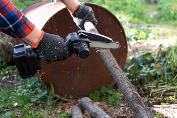 A man in gloves saws a wooden tree trunk with a saw.