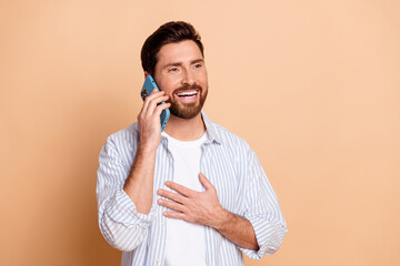 Smiling young man showing joyful expression while having a phone call against a beige background