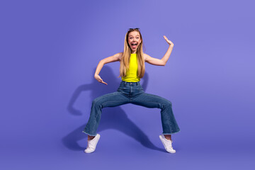 Energetic girl in casual outfit performing expressive pose against vibrant purple background showcasing cheerful and trendy lifestyle