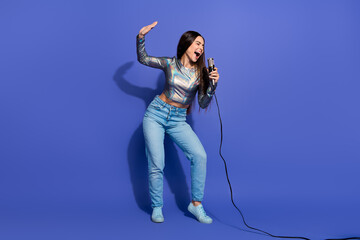 Young woman singing passionately into a microphone in a stylish metallic top and jeans against a...