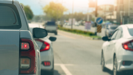 Fototapeta premium Rear side of pickup car white color. Turn on brake light. Cars are stopped at traffic lights at intersections. Background of trees side and green grass center of road.