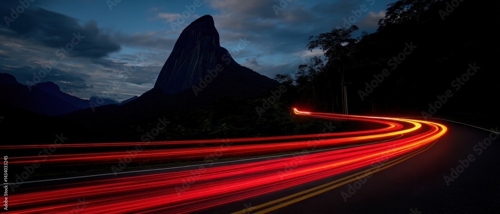 Poster dynamic light trails illuminate a winding road beneath a towering mountain peak at twilight creating