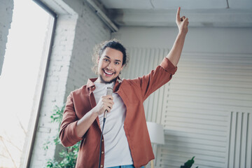Happy young man energetically singing into microphone with vibrant expression in brightly lit modern living space during daytime
