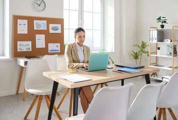 Businesswoman browsing laptop screen, boss woman sitting at workplace in office, uses corporate devices and business application, planning work, software information checking, employee surfing