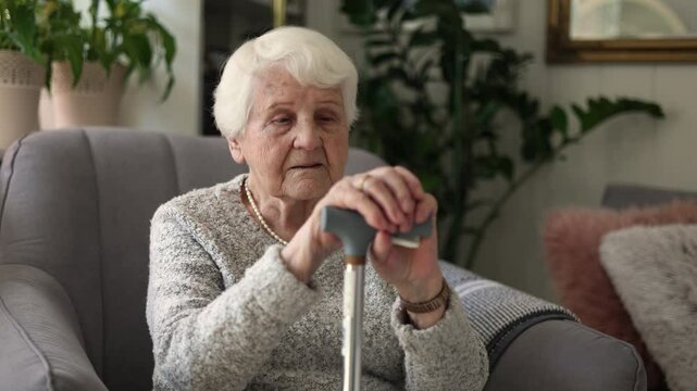 Elderly woman resting her hands on a cane while sitting in an armchair
