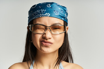 Confident young asian woman with glasses and a blue bandana expressing playful attitude indoors
