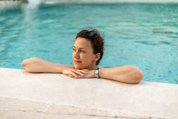 Woman relaxes by pool during sunny afternoon, enjoying calm water and peaceful atmosphere