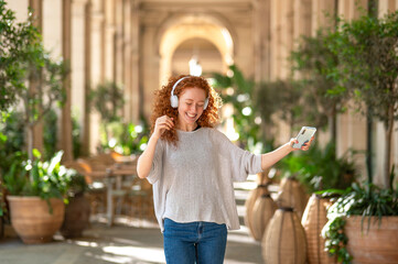 Happy redhead woman dancing with headphones and smartphone in a gallery