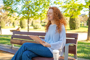 Smiling woman using tablet and relaxing on bench in park