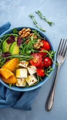 Appetizing salad with fresh avocado, tomato, cheese, arugula, and walnut served in bowl with fork on blue table, top view, healthy lifestyle, delicious meal