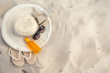 Relaxing beach essentials including a straw hat, sunglasses, flip flops, and sunscreen laid out on warm sand during a sunny day