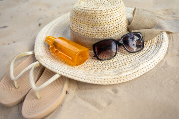 Summer beach essentials with hat, sunglasses, flip flops, and sunscreen on sandy shore