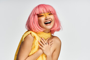 Joyful young asian woman with pink hair wearing bright yellow outfit expressing happiness