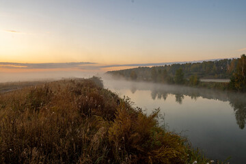 Morning fog on the lake at dawn. Colourful glow in the sky, with surrounding forest trees reflected...