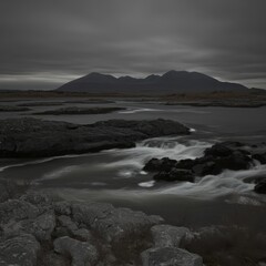Obraz premium Moody Grayscale River Landscape with Distant Mountains under a Cloudy Sky