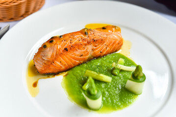 Beautiful salmon steak on a plate, served with fruit juice sauce and vegetable soup.