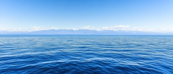 Obraz premium Serene seascape featuring gentle ocean waves under a clear blue sky with distant mountain range offering a tranquil and calming visual experience for viewers