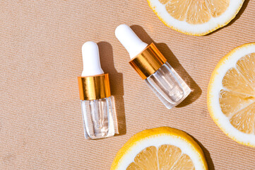 Two transparent serum dropper bottles with golden caps placed on textured beige background, surrounded by fresh lemon slices. Clean, elegant skincare flat lay for beauty and citrus-themed ads