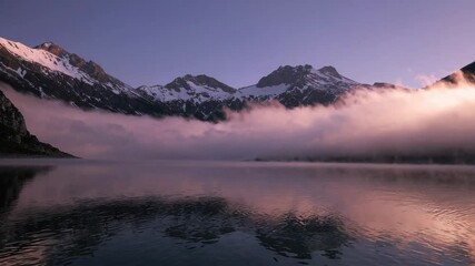 Serene mountain lake at sunrise with moving mist and snowcapped peaks