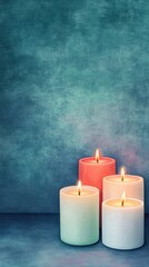 A serene arrangement of four lit candles in soft pastel colors against a textured teal background, creating a calming ambiance.