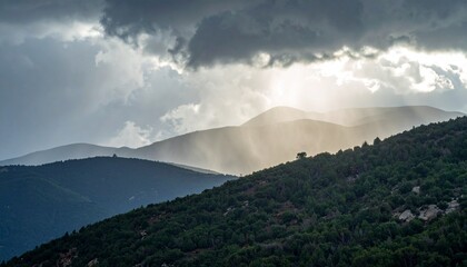 Obraz premium Rain falling over a mountain ridge under thick storm clouds as sunlight breaks through in the distance