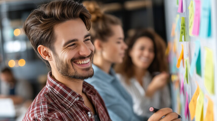 Fototapeta premium Happy young man working on project with sticky notes in office